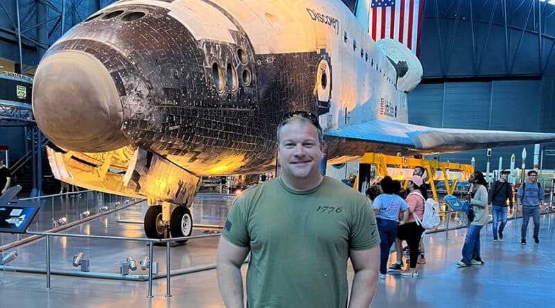 A man stands in front of a space shuttle orbiter on display at a museum.